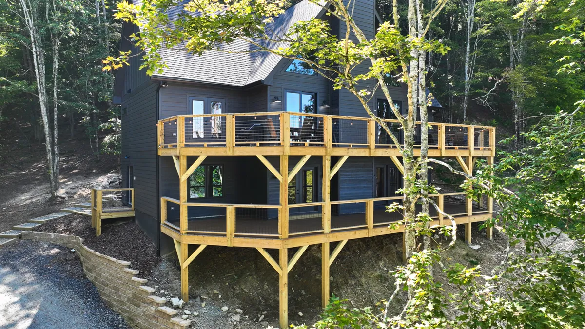 A tranquil wooden deck surrounded by trees, with dark exterior walls hinting at the home's rustic charm. The deck provides a generous space for outdoor living, well-suited for relaxation, socializing, or simply enjoying nature from the comfort of the home.