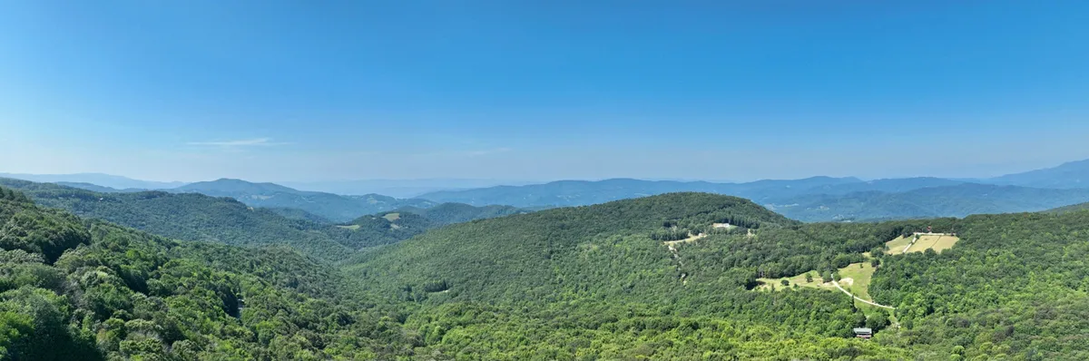 A sweeping mountain view with rolling hills, dense forest, and distant peaks under a clear blue sky. The untouched natural landscape invites activities like hiking, wildlife watching, and quiet reflection, echoing the year-round appeal of Beech Mountain.