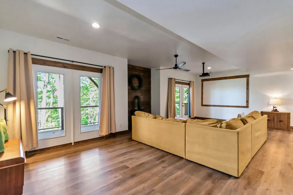 A spacious living area with a large sectional couch, windows that offer views of lush greenery, and warm wooden accents. The space is inviting and comfortable, suggesting a welcoming environment for both people and pets after a day of exploring the outdoors.