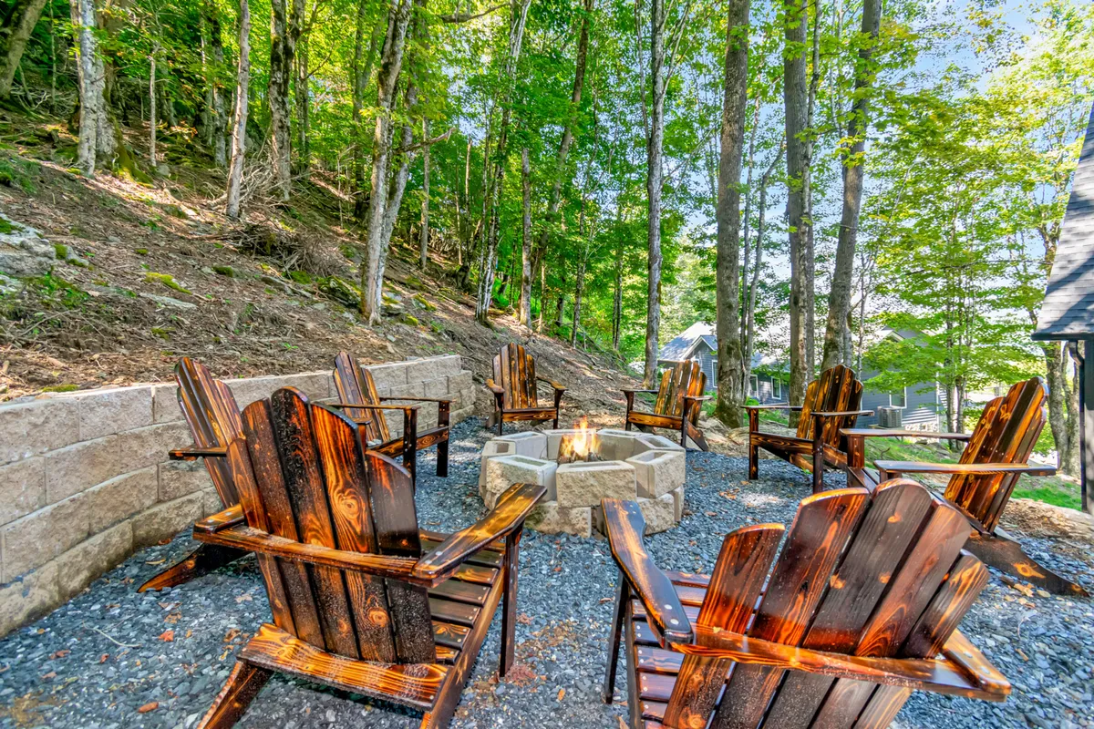 A wood-burning fire pit encircled by wooden chairs, set amidst tall trees. The cozy setup is designed for gathering, storytelling, and experiencing the great outdoors, with hints of the sky above suggesting stargazing potential.