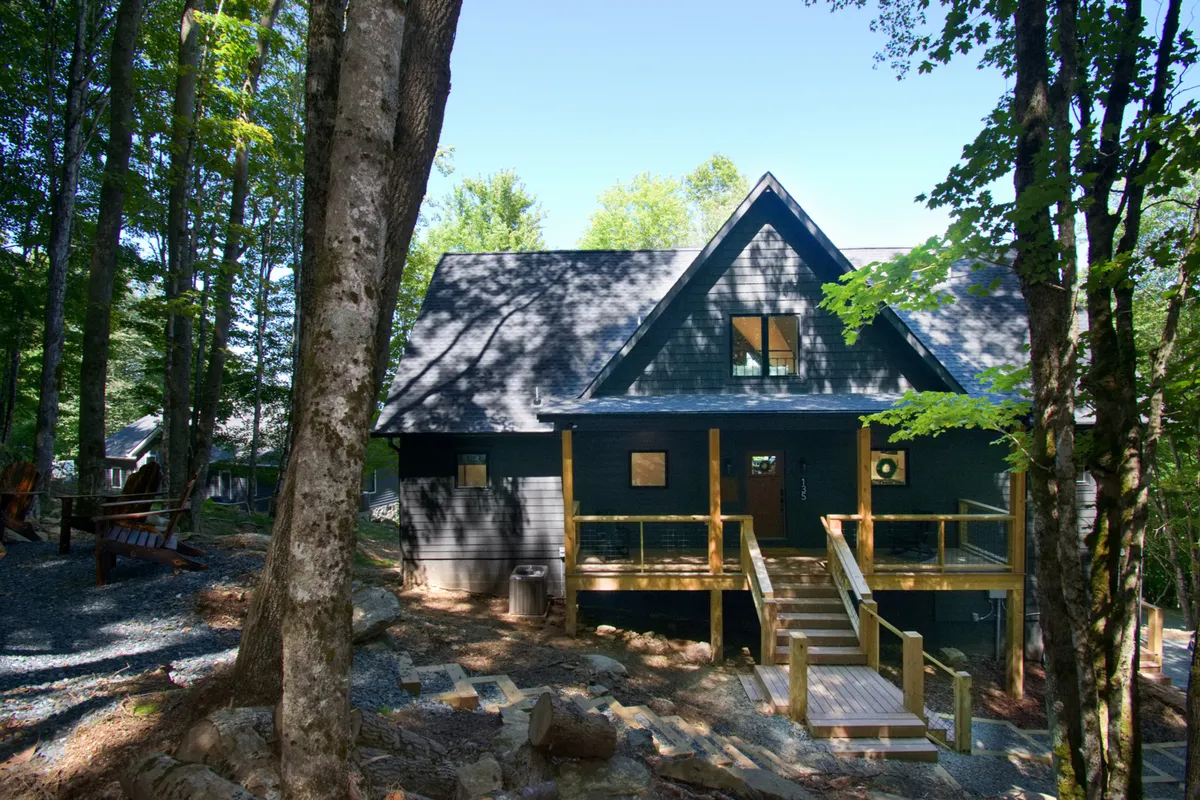 The spacious wooden deck is surrounded by mature trees, with large windows connecting the interior to the outdoors. The deck offers ample space for outdoor gatherings, relaxation, or family barbecues, embodying the promise of adventure and togetherness.