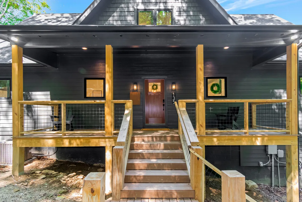 This image features the inviting front porch of Beech Blessings, showcasing wooden steps, a decorative wreath on the front door, and cozy seating that suggests a warm welcome. The setting sun casts a gentle glow, adding to the welcoming ambiance.