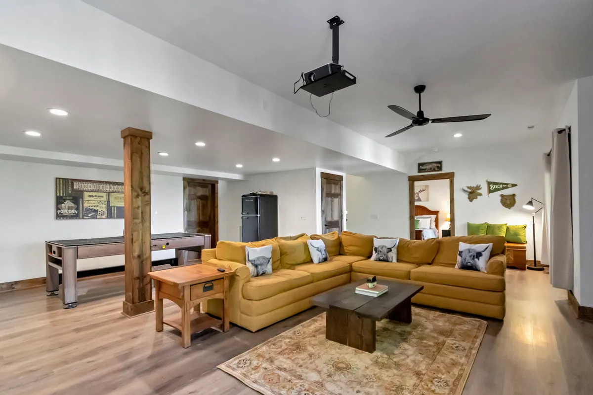 This image presents a vibrant, inviting game room with a yellow sectional couch, a coffee table, a central game table, and decorative wall art. The space is designed for relaxation, socializing, and playful competition, reflecting a lively and comfortable atmosphere.