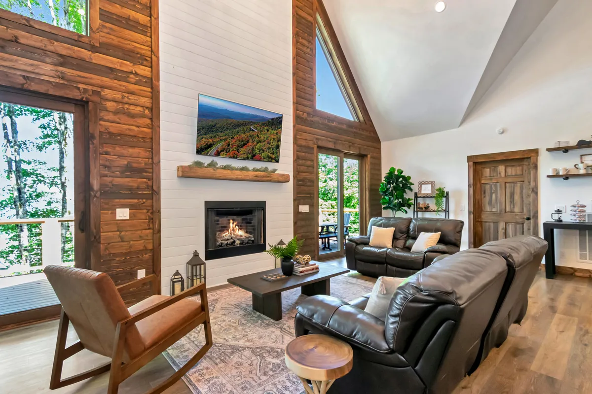 The living room features a cozy fireplace, large windows offering views of the mountains, and plush, comfortable seating arranged for conversation and relaxation. Artistic decor and warm lighting create an inviting, homey atmosphere.